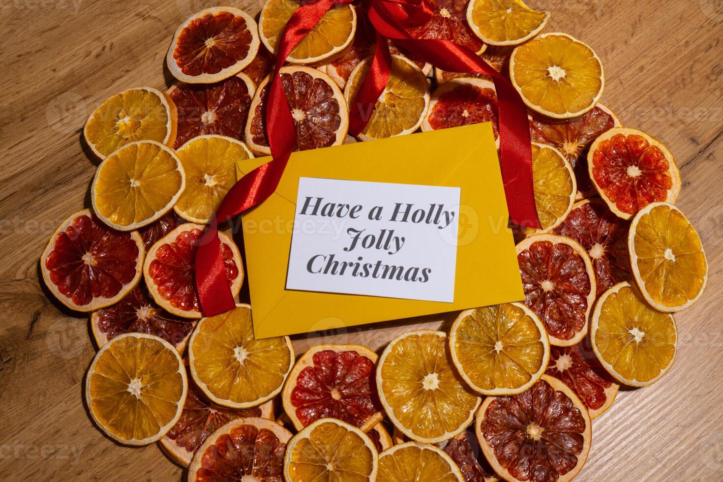 Christmas handmade wreath made of dried slices of orange and grapefruit with yellow envelope and paper note with HAVE A HOLLY JOLLY CHRISTMAS text. Winter holiday celebration greeting card. top view photo