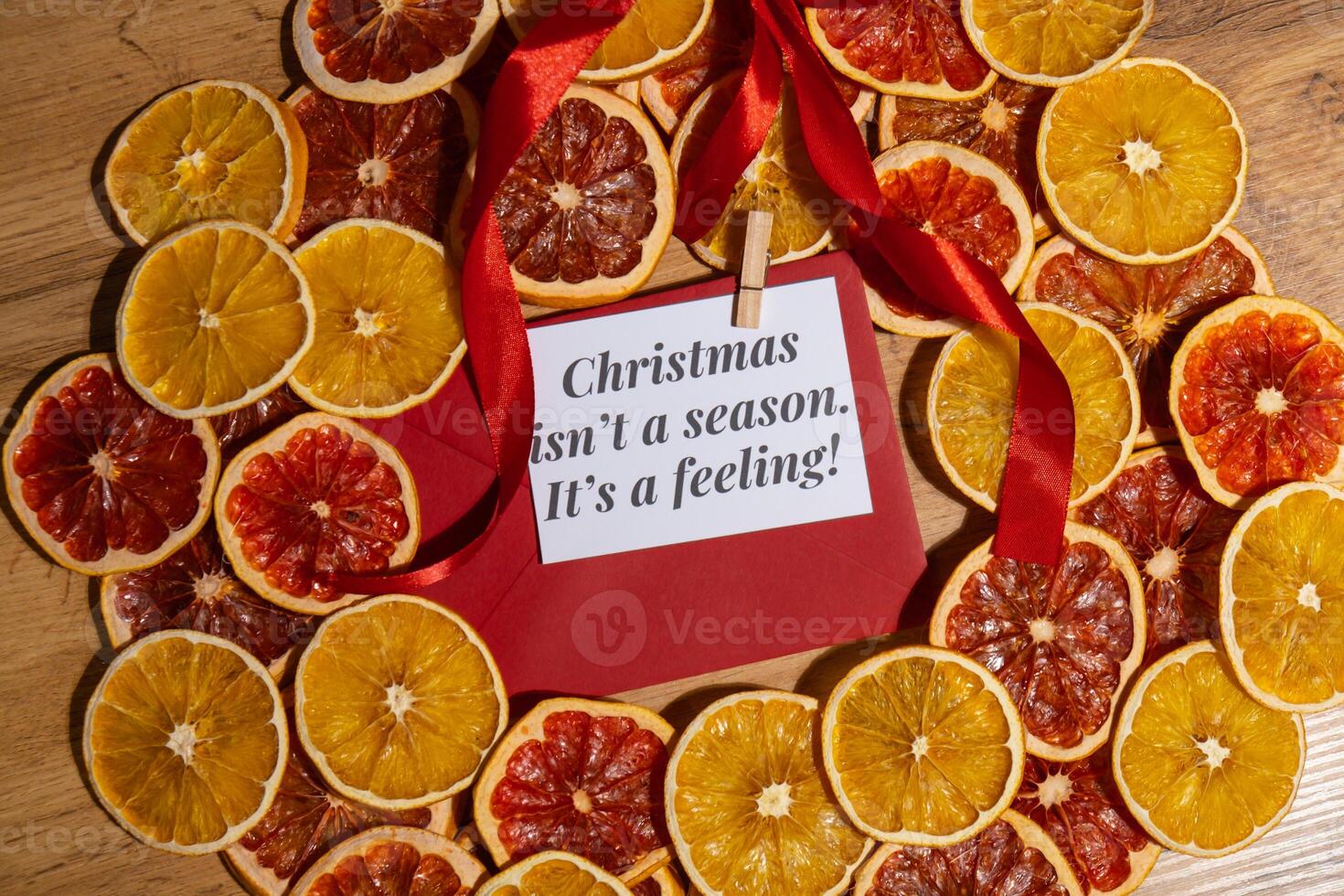 Christmas handmade wreath made of dried slices of orange and grapefruit with red envelope and paper note with CHRISTMAS ISN'T A SEASON IT'S A FEELING text. Winter holiday celebration greeting card. top view photo