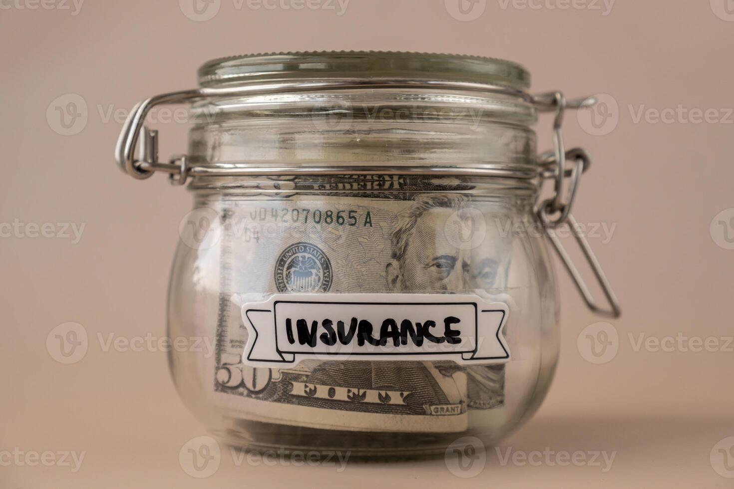 Saving Money In Glass Jar filled with Dollars banknotes. INSURANCE transcription in front of jar. Managing personal finances extra income for future insecurity. Beige background photo