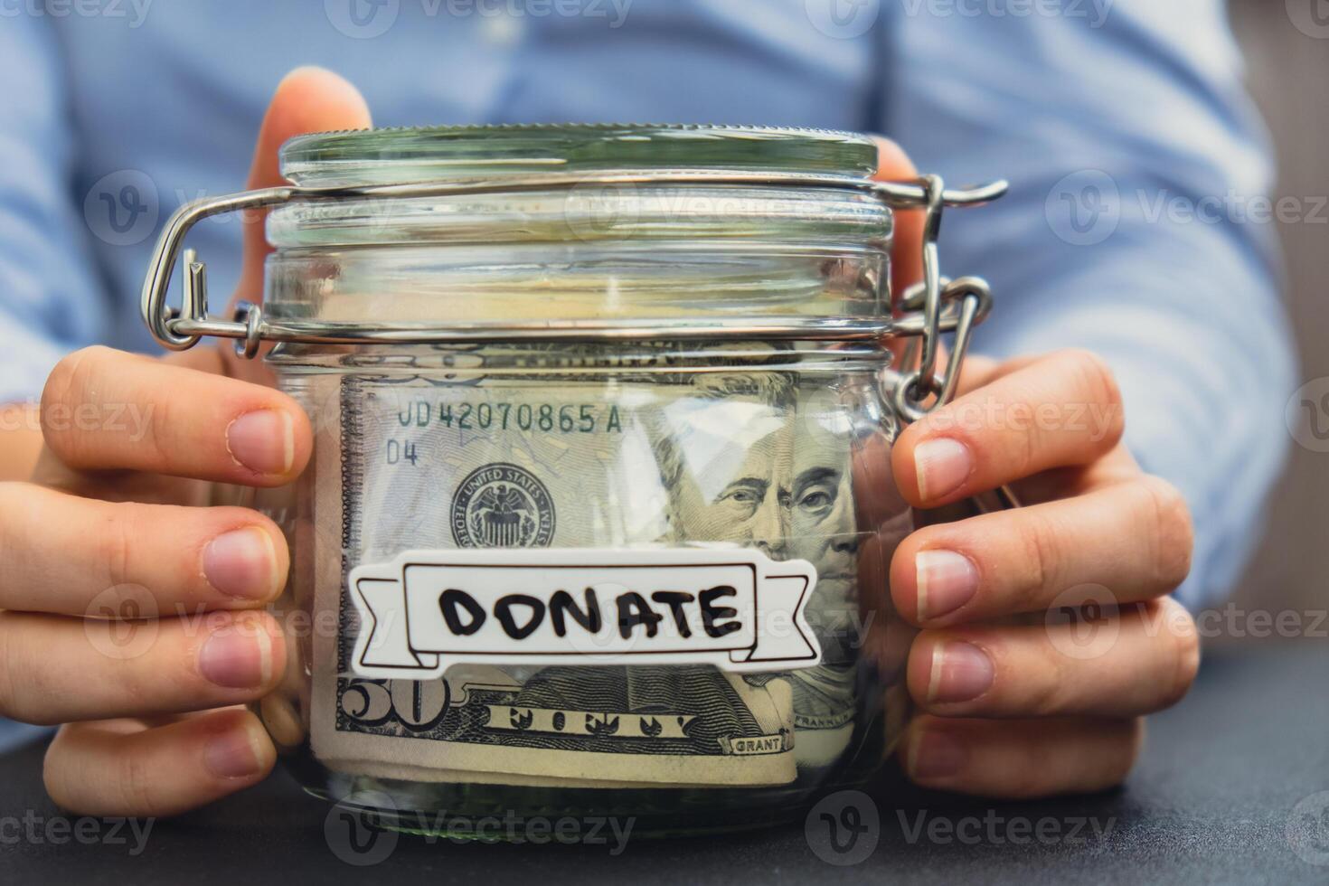 Female hands Saving Money In Glass Jar filled with Dollars banknotes. DONATE transcription in front of jar. Managing personal finances extra income for future insecurity background photo