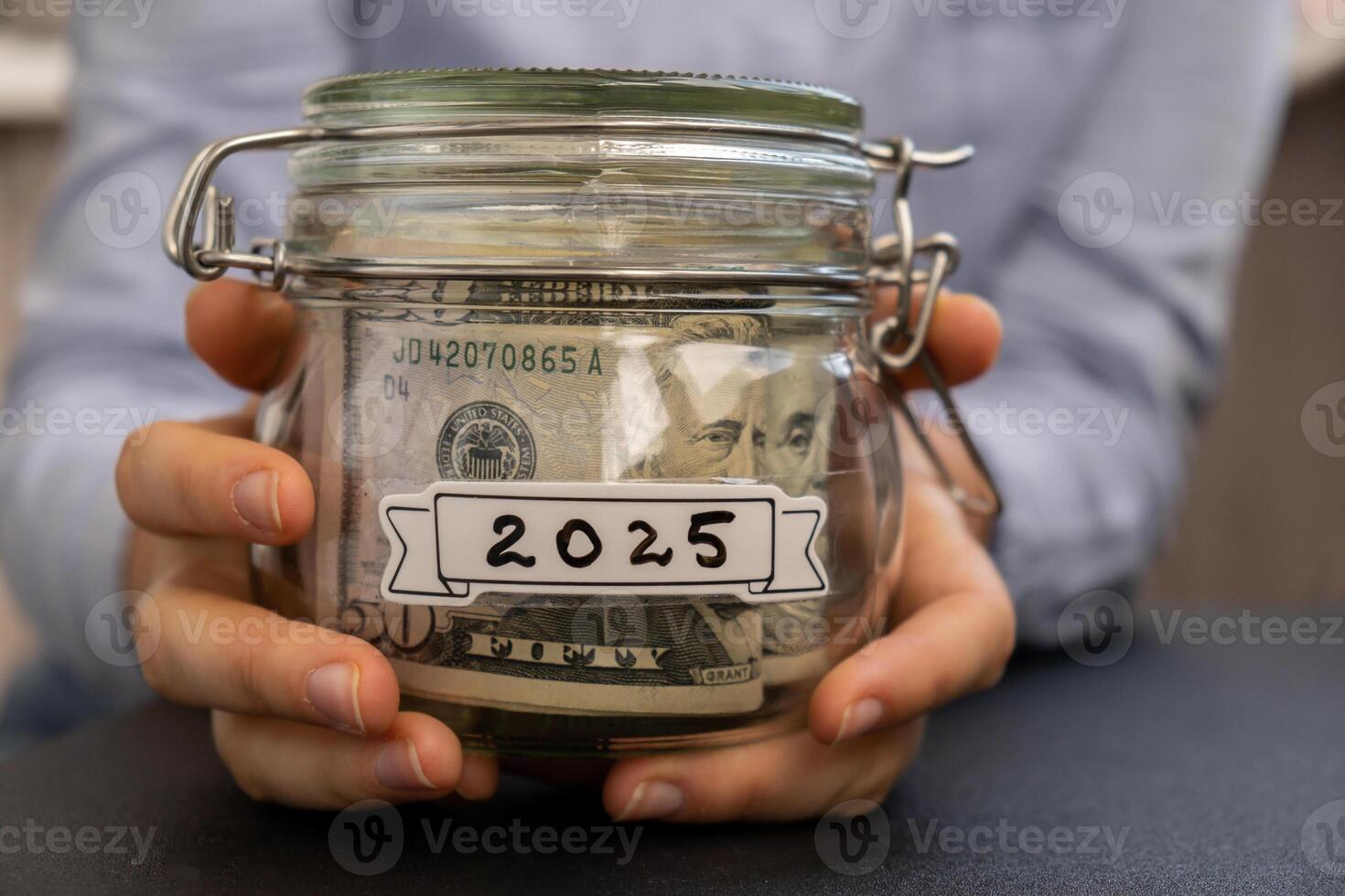 Unrecognizable woman holding Saving Money In Glass Jar filled with Dollars banknotes. 2025 year transcription in front of jar. Managing personal finances extra income for future insecurity background photo