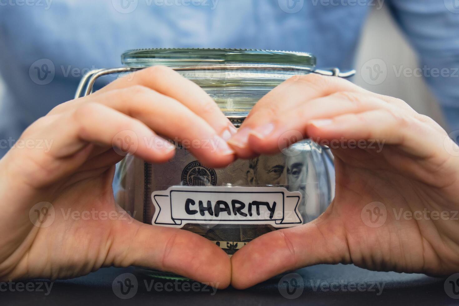 Female showing heart sign with hands Saving Money In Glass Jar filled with Dollars banknotes. CHARITY transcription in front of jar. Managing personal finances extra income for future insecurity background photo