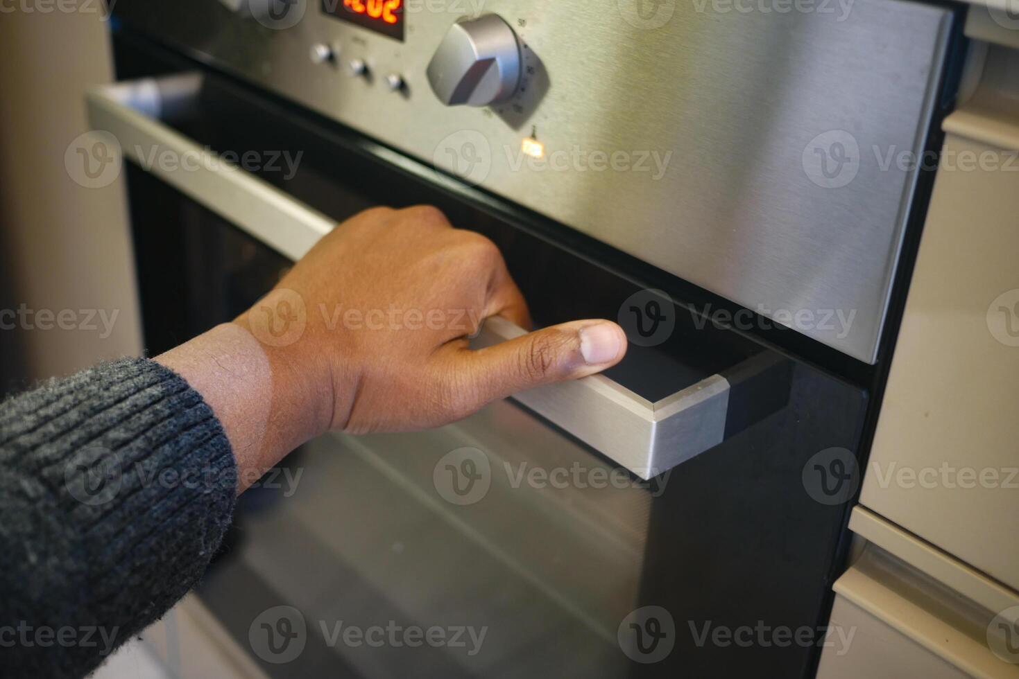 A person is using their hand to open a modern oven, engaging in culinary activities at home photo