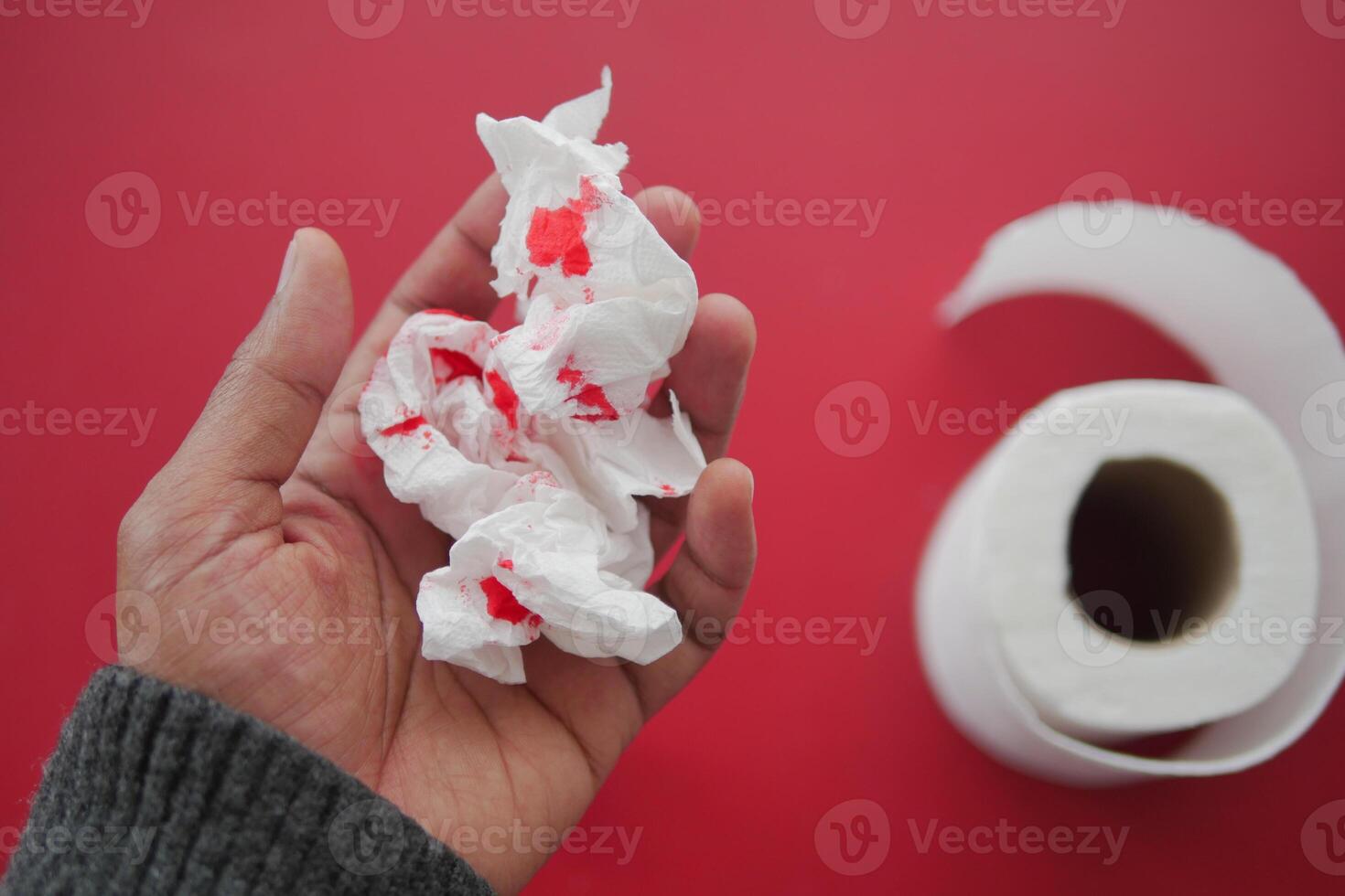 A blood spot is noticeable on a tissue next to a roll of toilet paper in the background photo