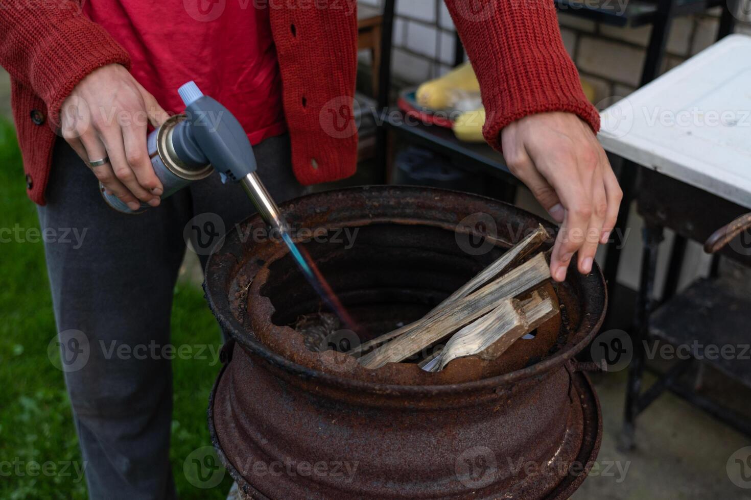 A man sets fire to firewood with a gas burner in a barbecue, in the evening photo