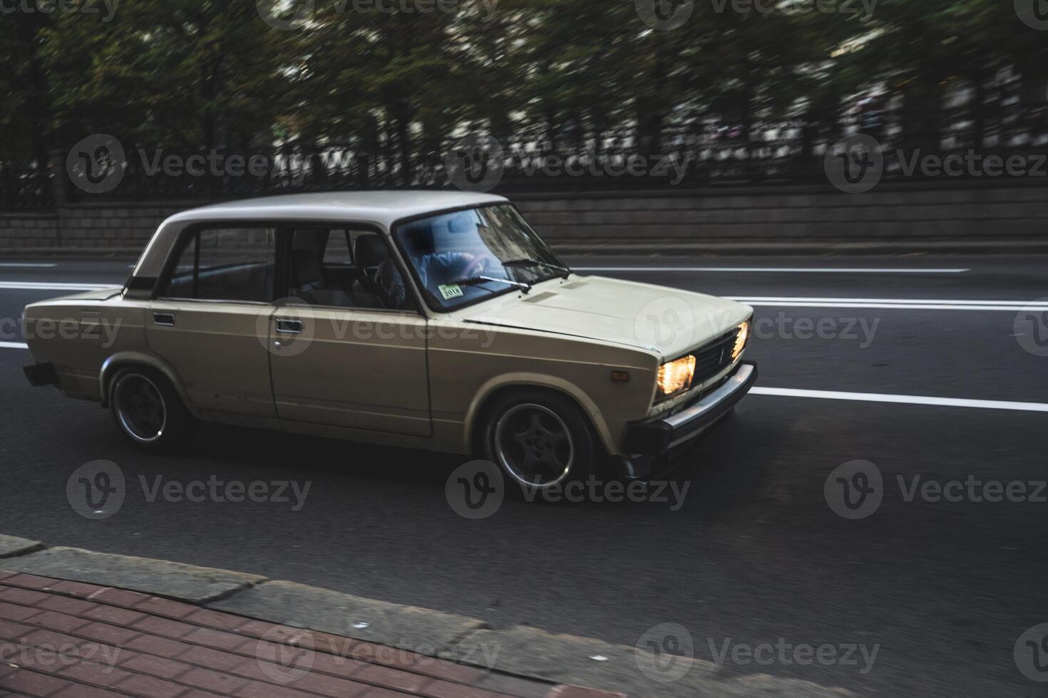 An old, Soviet, tuned car is driving in the evening in the city photo