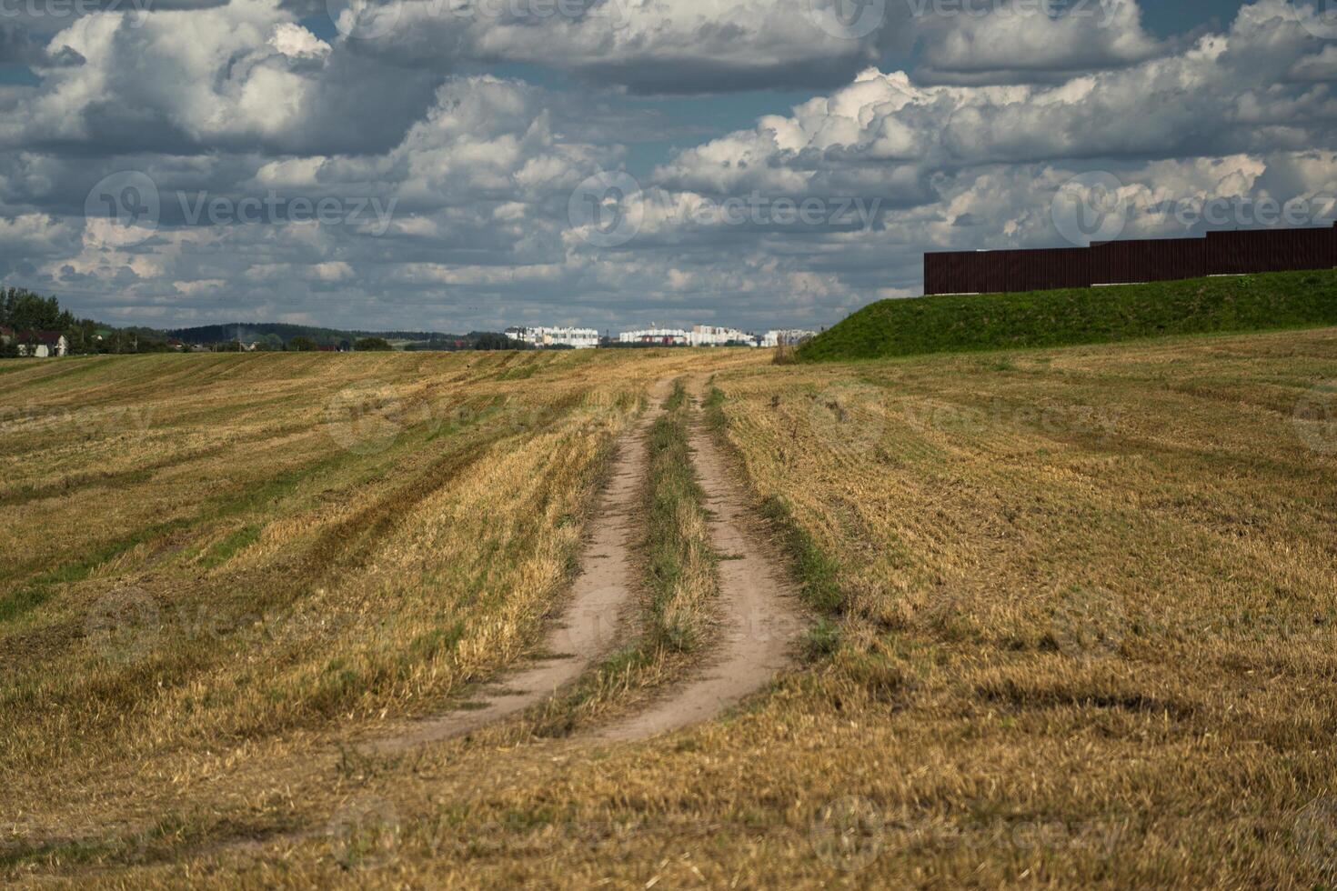 Thick clouds over a dirt road in a field. The road to the field after harvest photo