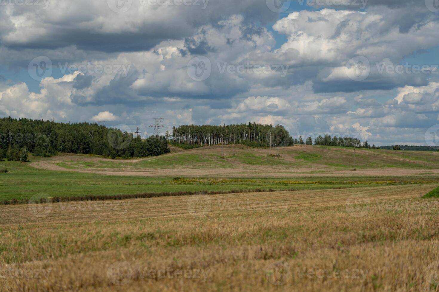 Thick clouds are flying low in the sky over green and yellow fields photo