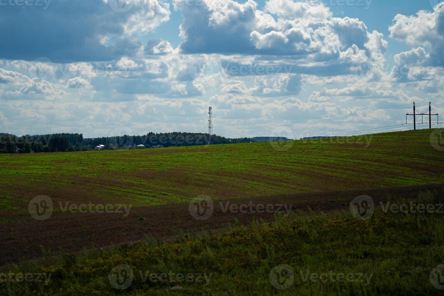 Thick clouds over green fields. The highway is far beyond the field photo