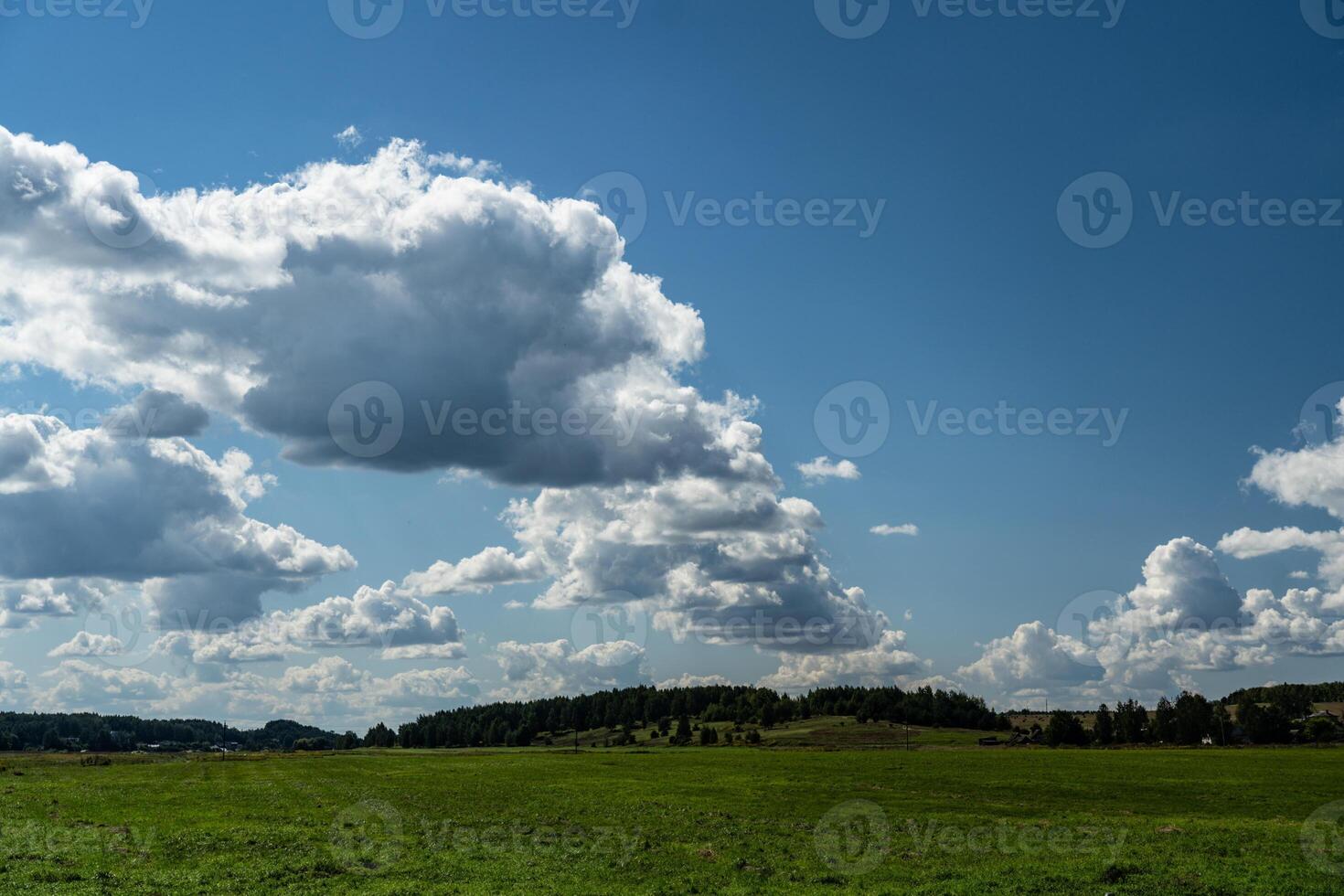 Thick clouds over green fields. The highway is far beyond the field photo