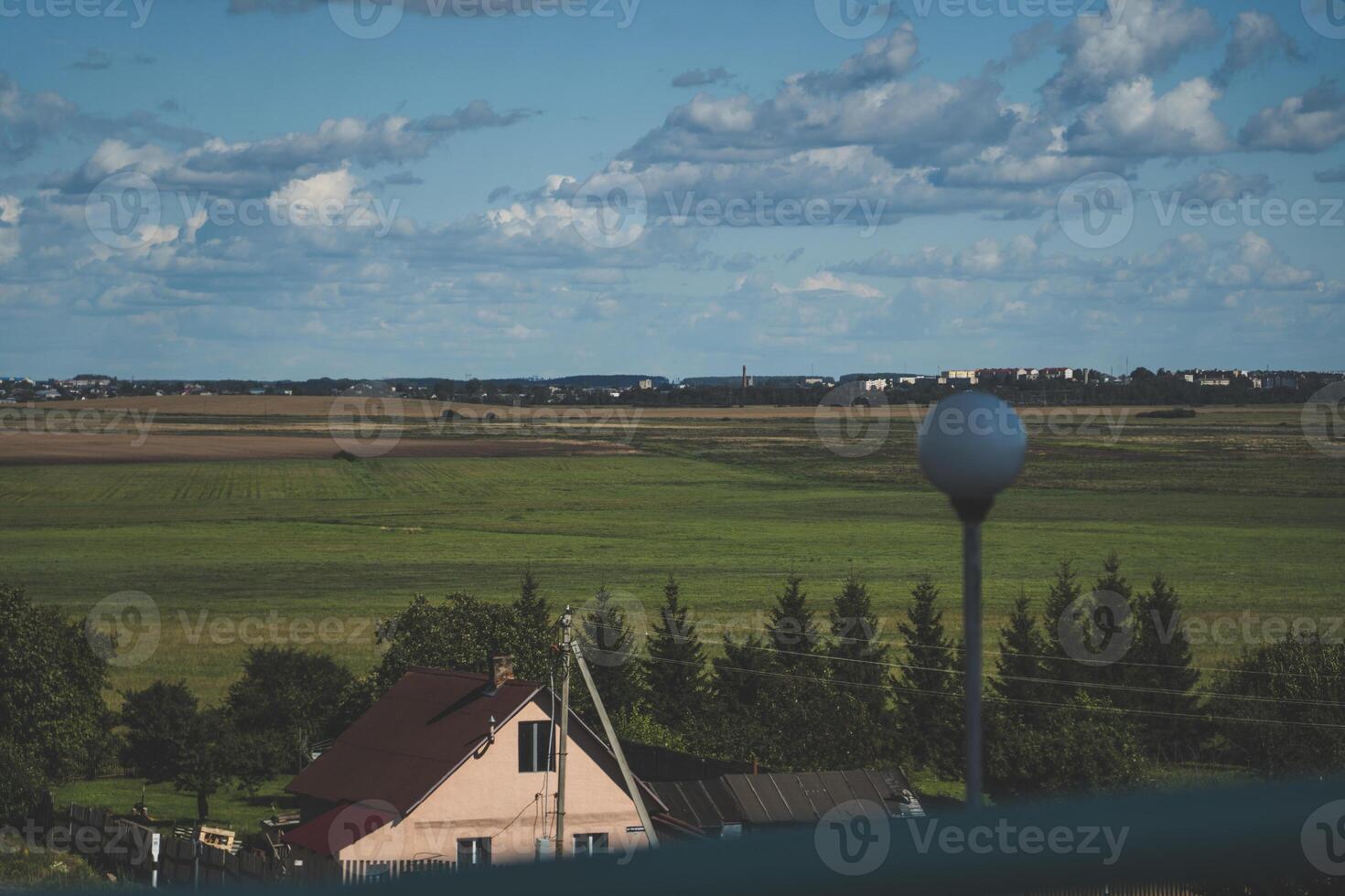 A village house, and behind it a large, green field. Thick clouds in the sky photo