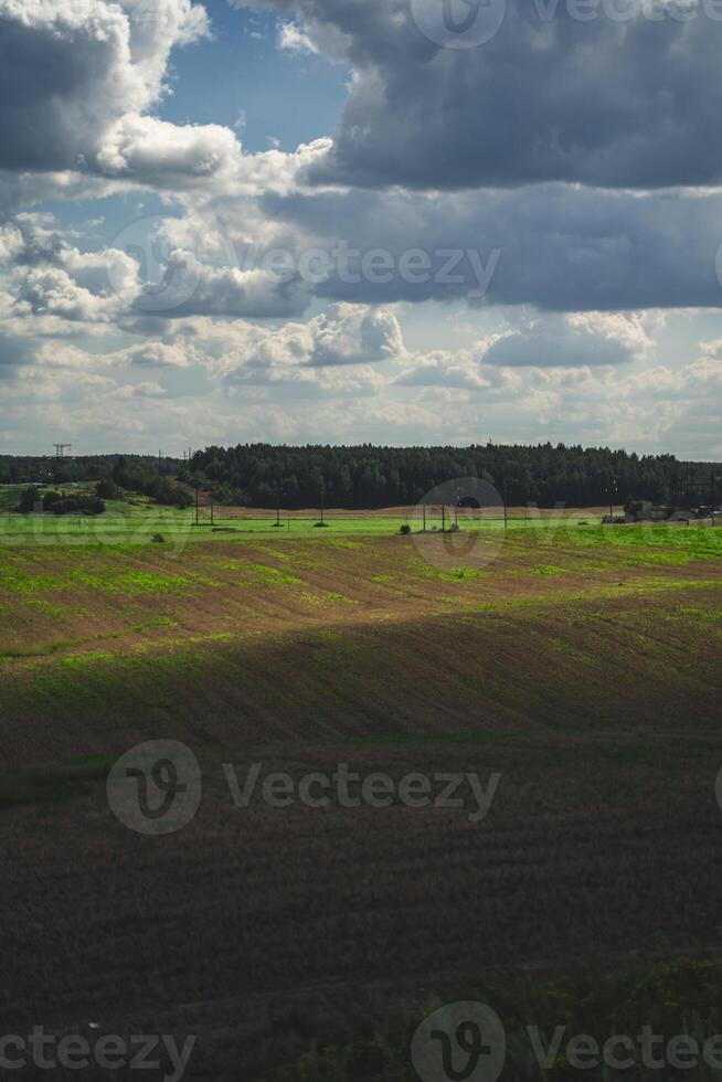 Thick clouds over green fields. The highway is far beyond the field photo