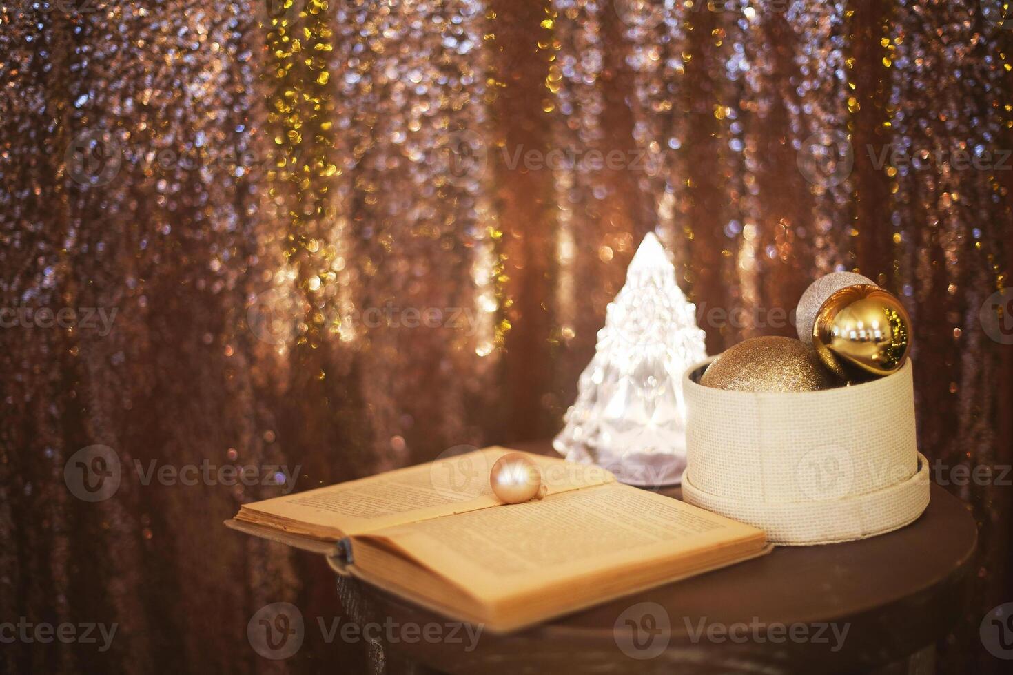 Little box with a lot of Christmas silver and golden decorations near the Christmas tree lamp and the book photo