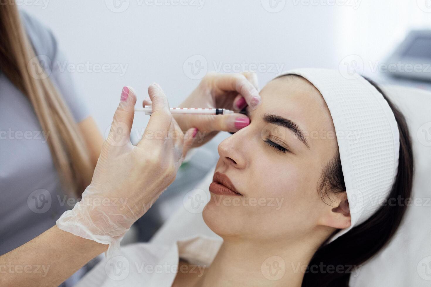 Female cosmetologist in transparent gloves makes an injection in the lower jaw of her client photo