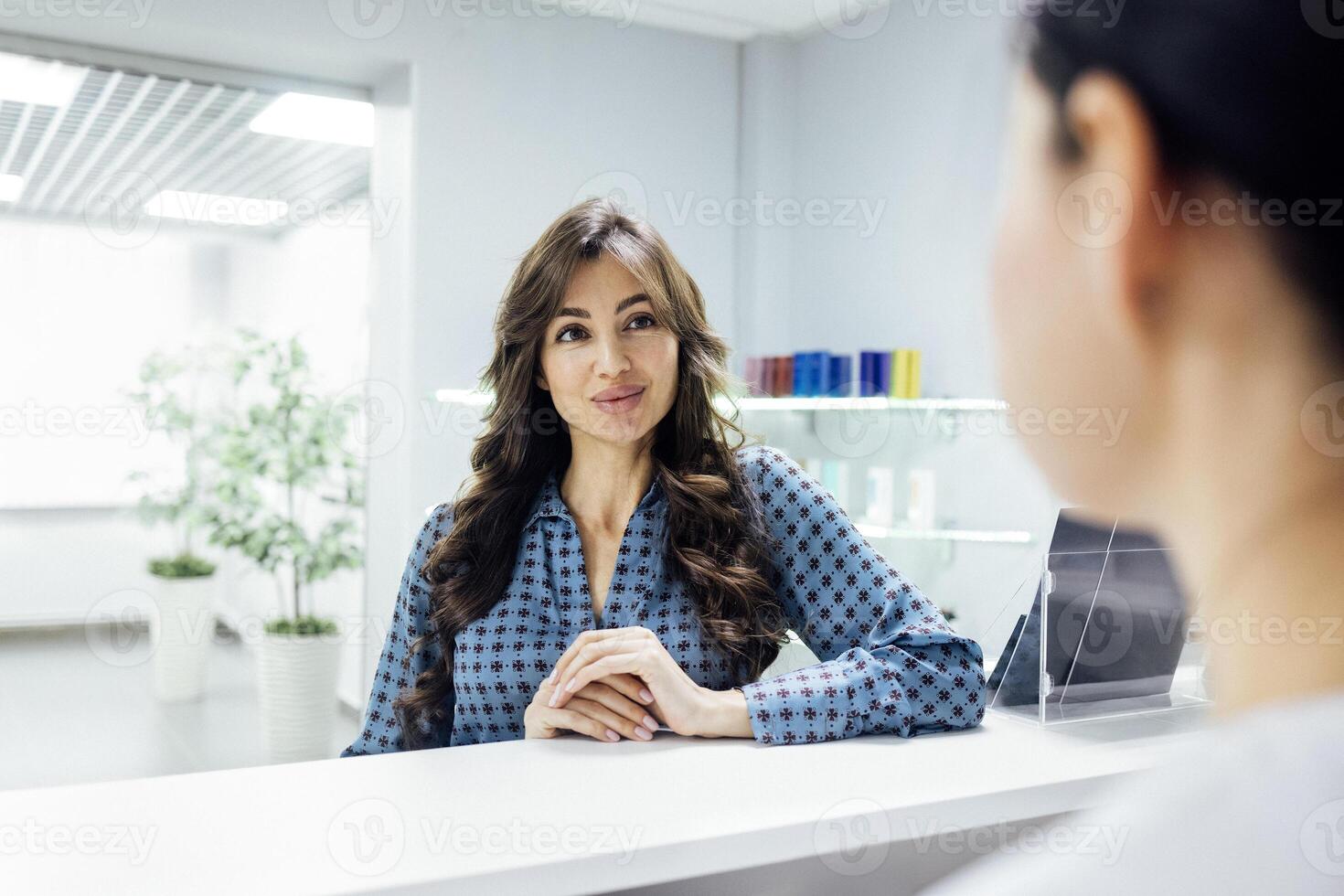 Smiling female client communicates with reception woman in a beauty salon. Young pretty caucasian girl signs up for a spa treatment. photo