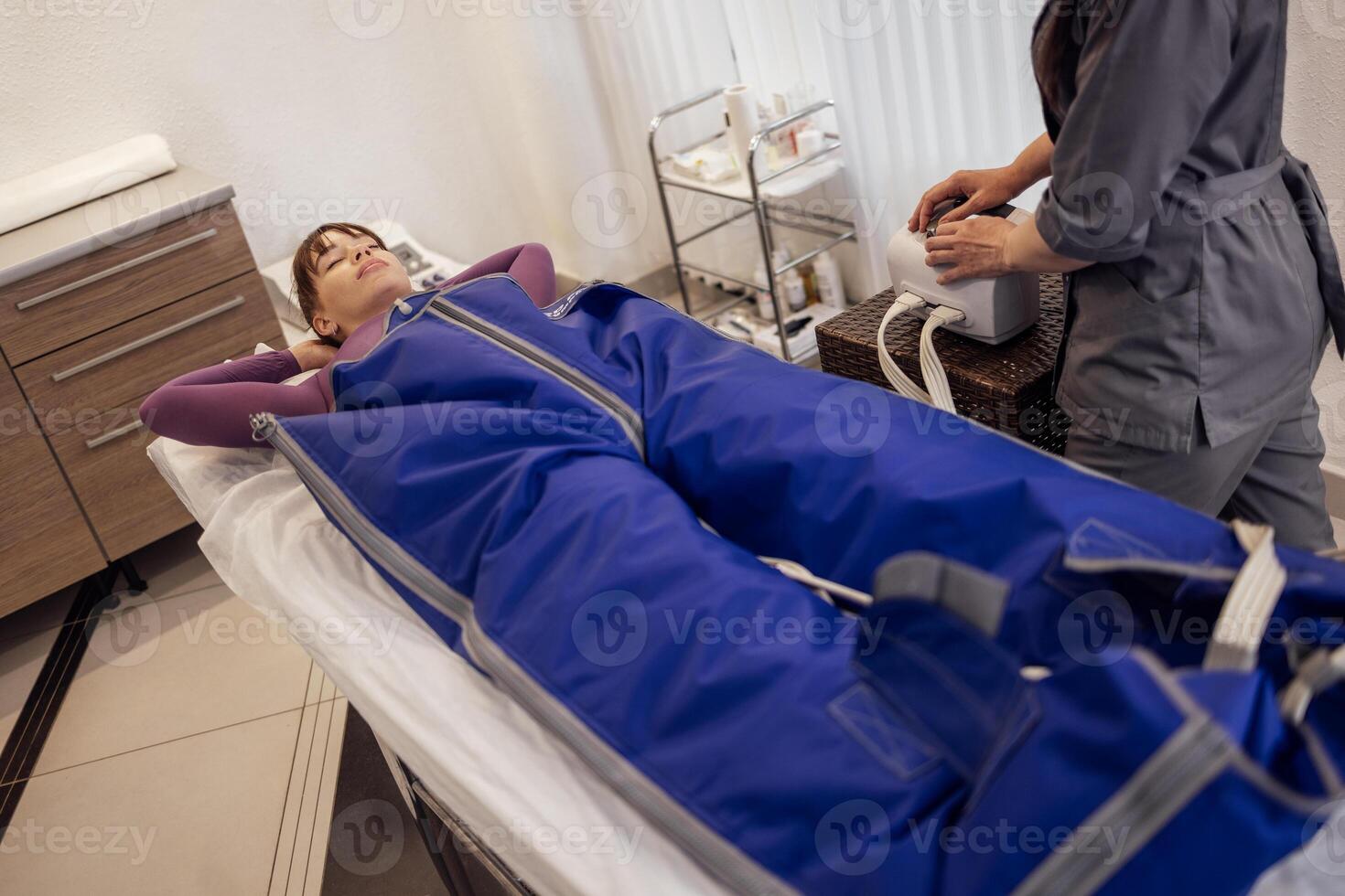 Young attractive woman lies with her hands behind her head in a special suit during pressotherapy. photo