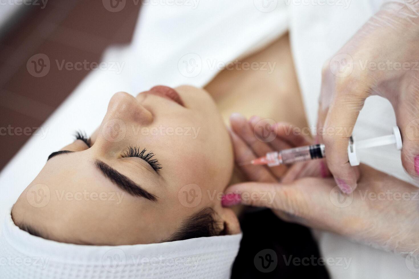 Beauty injections. Female cosmetologist in transparent gloves makes an injection in the lower jaw of her client. photo