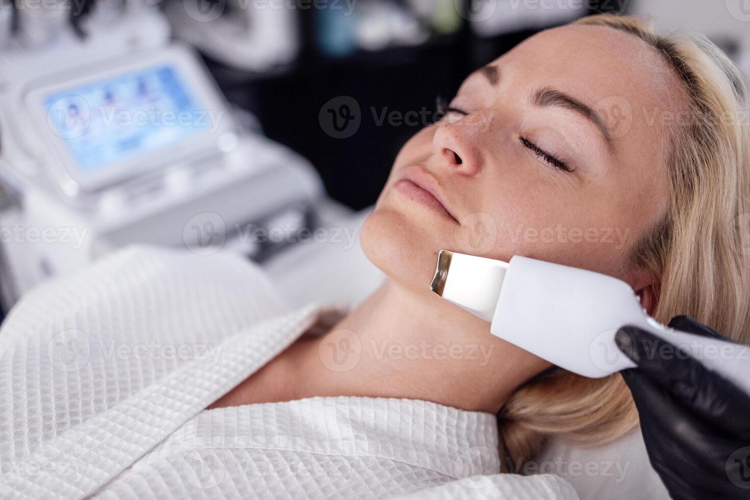 Beauty master makes ultrasonic facial peeling to her client. photo