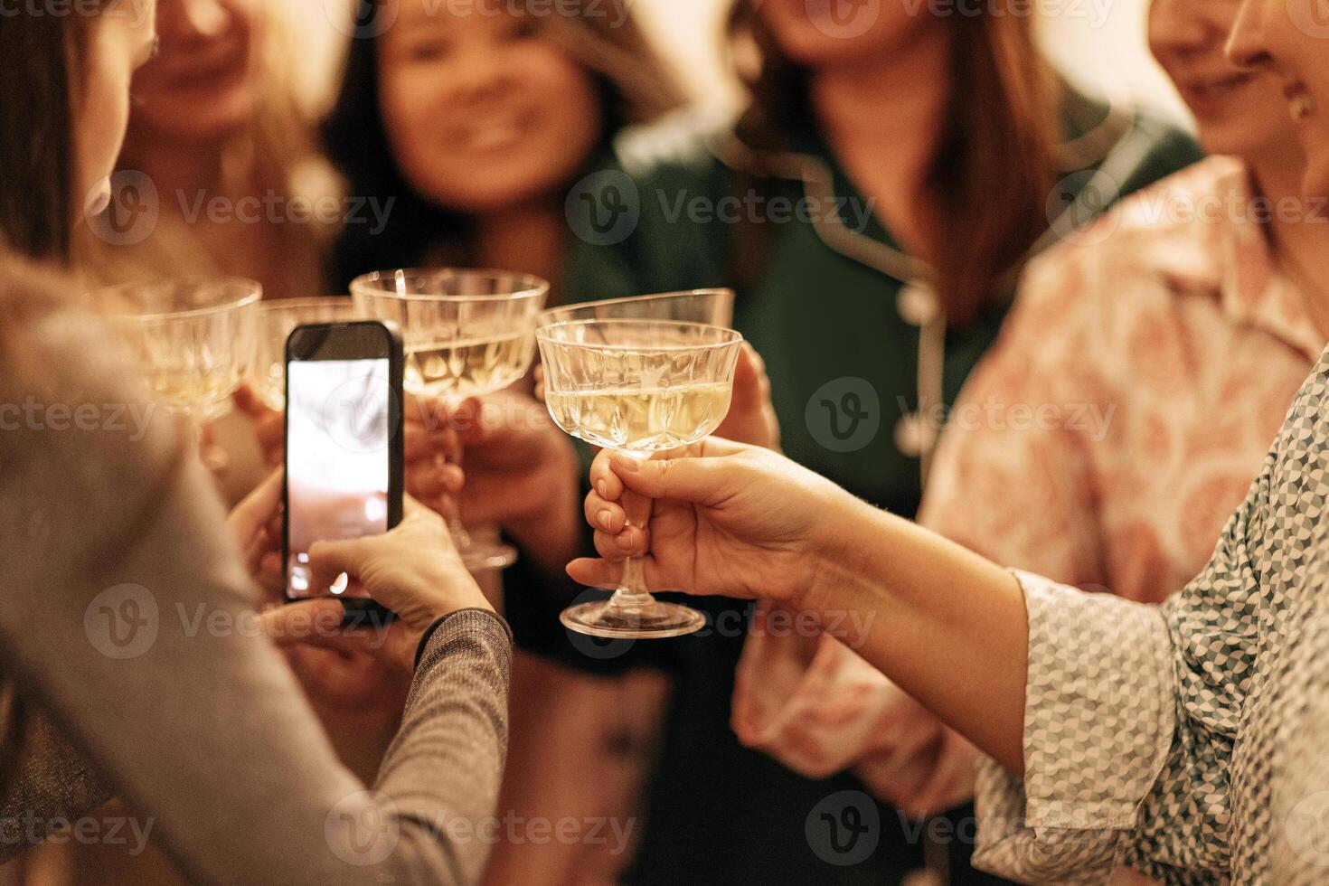 Close-up of a female hands holding a phone and toasting with glasses of champagne. A young woman takes a photo of cups with sparkling wine. A festive meeting of friends.