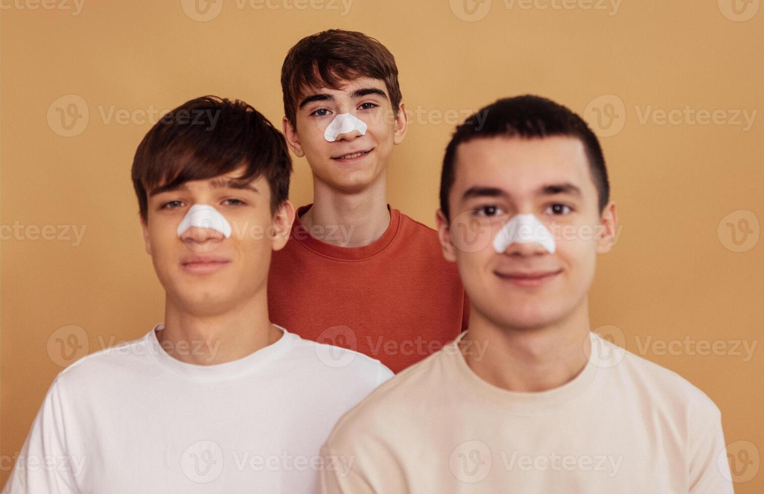 Portrait of teenagers with cleansing strips on their noses to remove black dots. Three boys take care of the skin of the face. Cosmetic procedure. Man beauty routine. photo