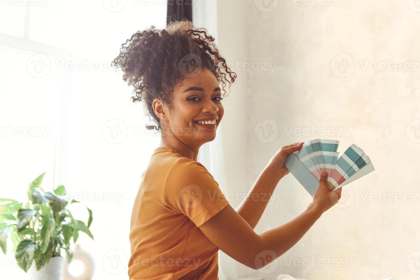 Smiling African American girl stands back to camera in middle of bed room with palette of blue shades for interior renovation. photo