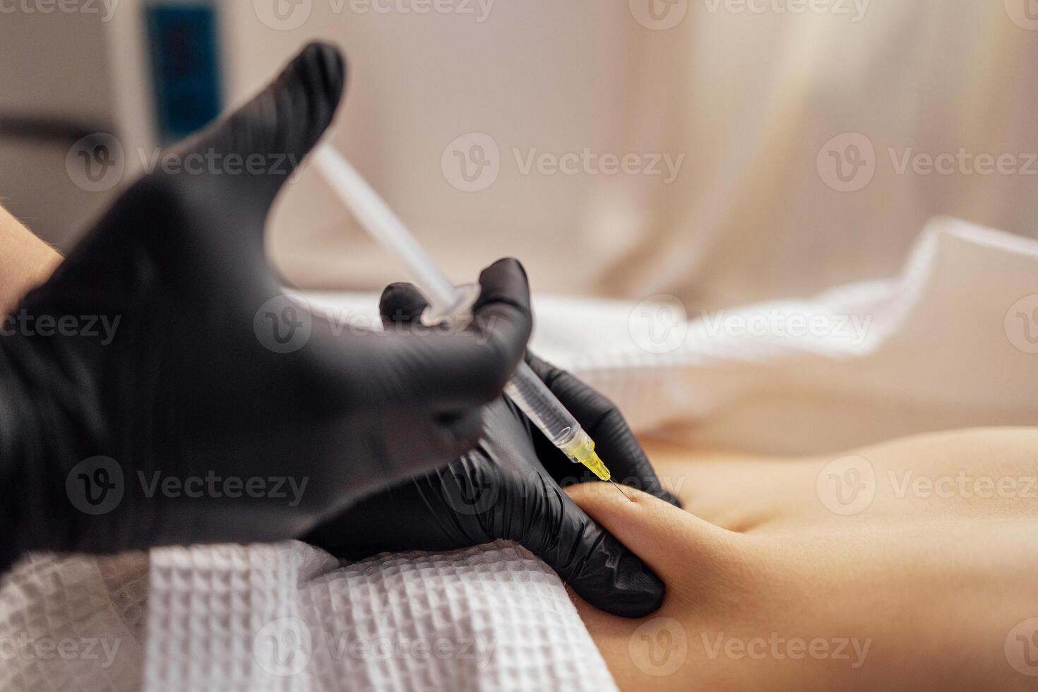 Close up of hands in black gloves of cosmetologist giving injection into stomach of client. photo
