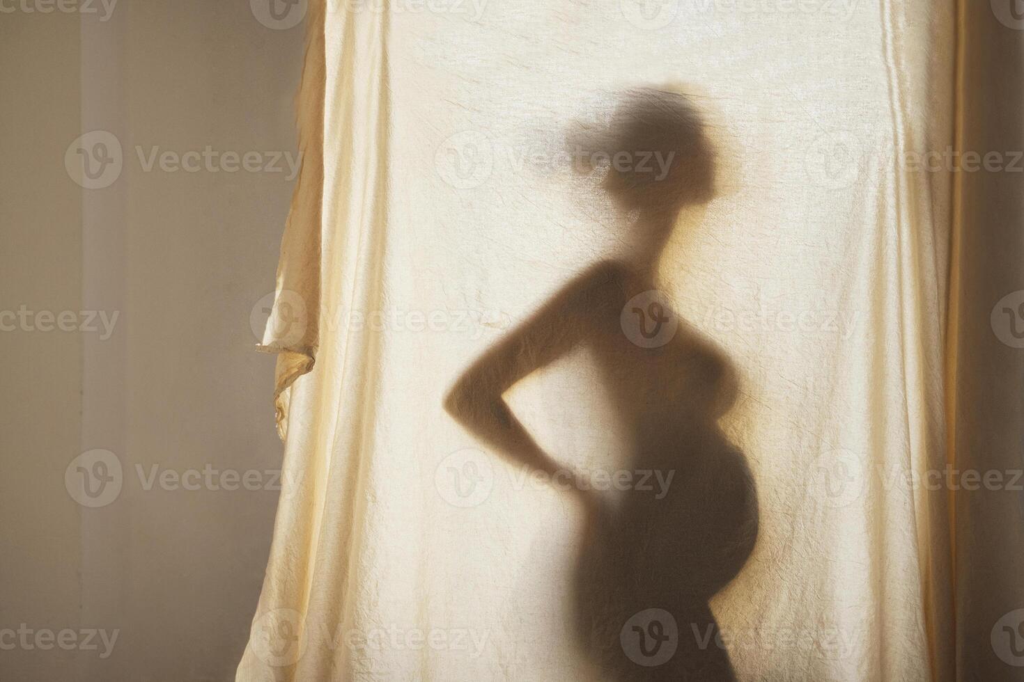 Shadow silhouette of a female pregnant behind a textured fabric photo