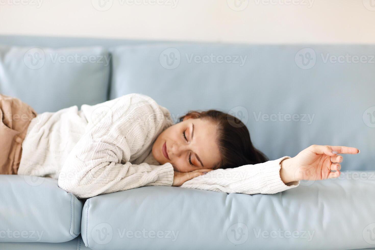 Close up of young Caucasian woman laying down on blue sofa indoor, fell asleep in casual outwear photo
