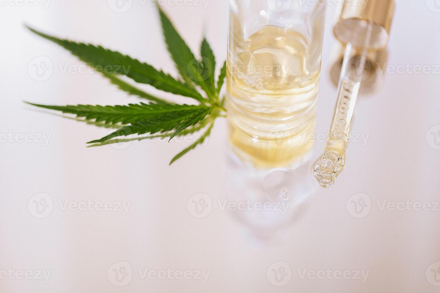 Mock up bottle cosmetic product and pipette with cannabis leaves on white glossy background. Yellow moisturizing facial serum with hyaluronic acid and hemp leaf on marble table. photo