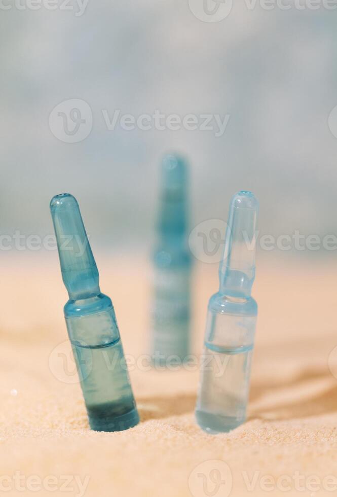 Blue ampoules with intense moisturizing concentrate with hyaluronic acid and vitamins on a background of sand. Set of facial serums with peptides and collagen. photo