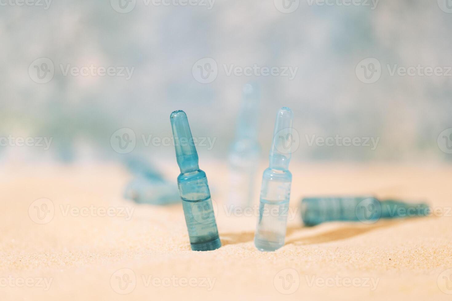 Blue ampoules with intense moisturizing concentrate with hyaluronic acid and vitamins on a background of sand. Set of facial serums with peptides and collagen. photo
