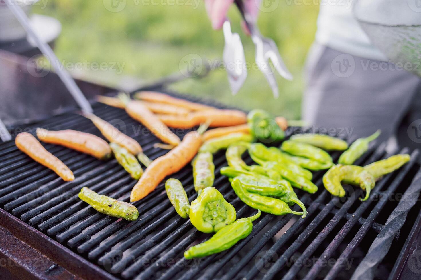 Close-up of a vegetarian barbecue and a cooking man. Tasty fried peppers and carrots on the grill. Vegetables are cooked on coals on the bars in the open air. photo