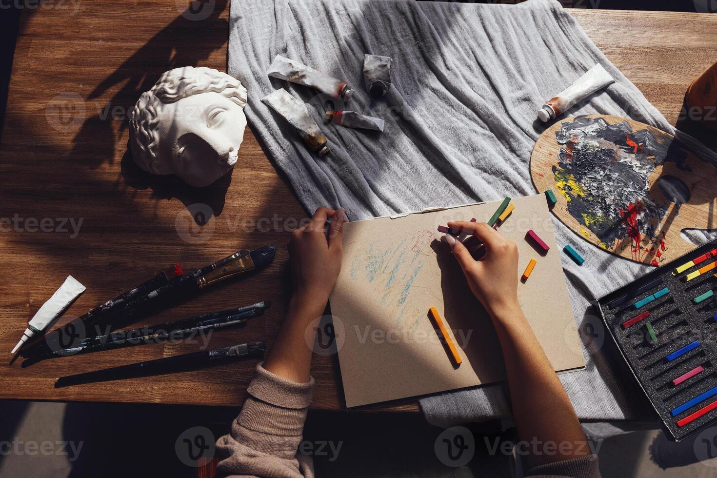 Young creative pretty african american girl artist paints with pastels while sitting at table in front of window photo