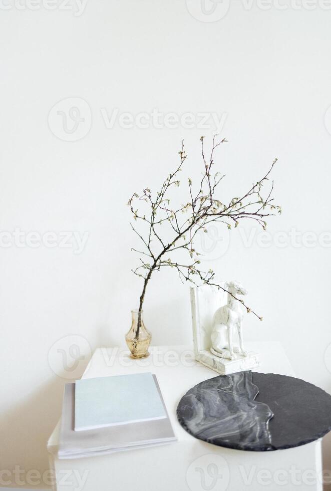 Square white wooden table with acrylic round painting, notebooks, glass transparent vase and tree branch, marble hound dog statue. photo