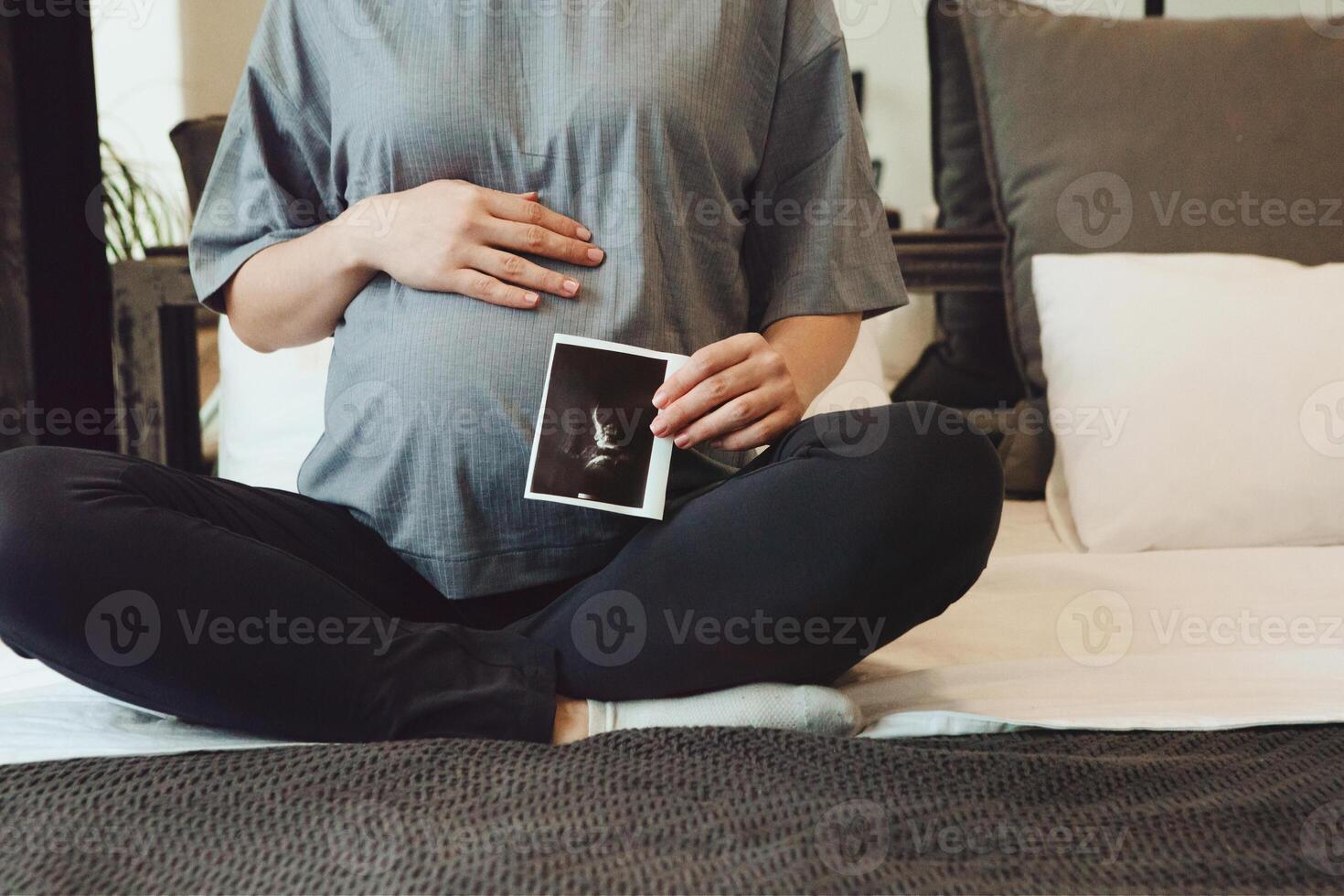 Cropped shot of pregnant woman holding pregnancy ultrasound or baby sonogram while sitting on bed photo