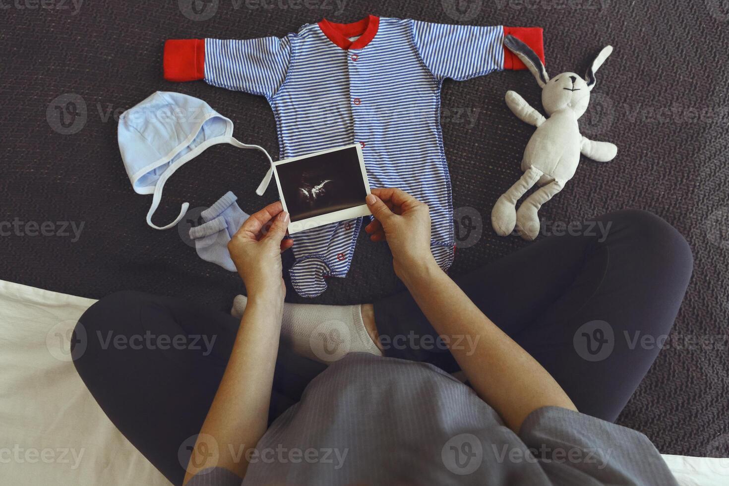 Pregnant woman looking at adorable newborn clothing while relaxing at home, preparing for childbirth photo
