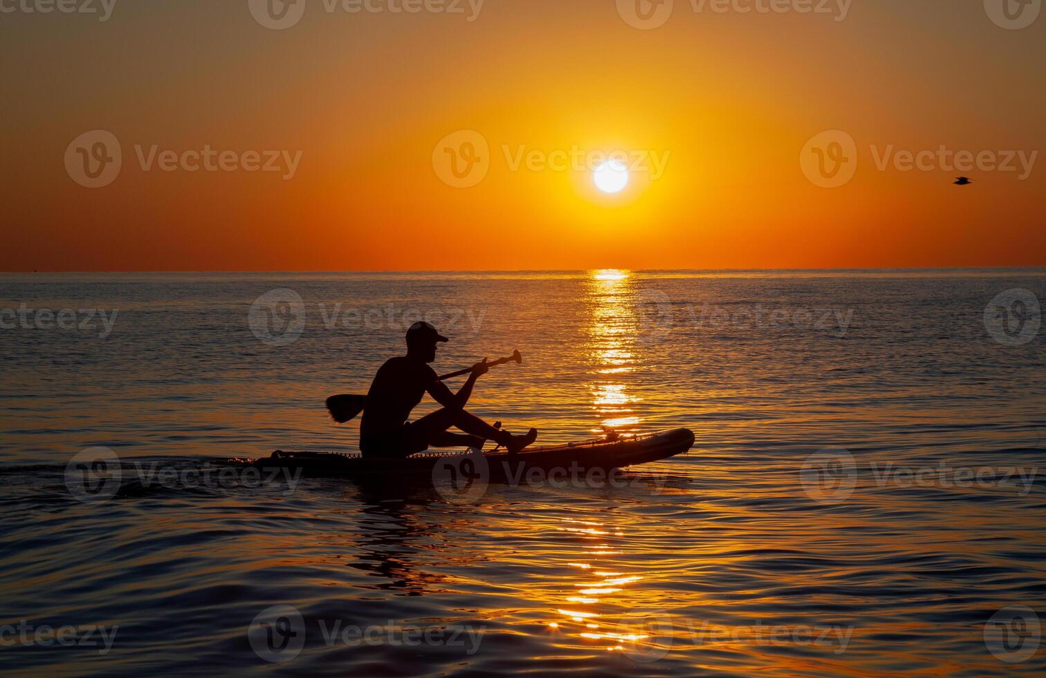 Silhouette of a man floating on a board with an oar. Dawn sun on the sea. Swimming on a supboard. Water active sports. Beautiful landscape. Sunset on the sea. Ocean coast. Copy space. photo