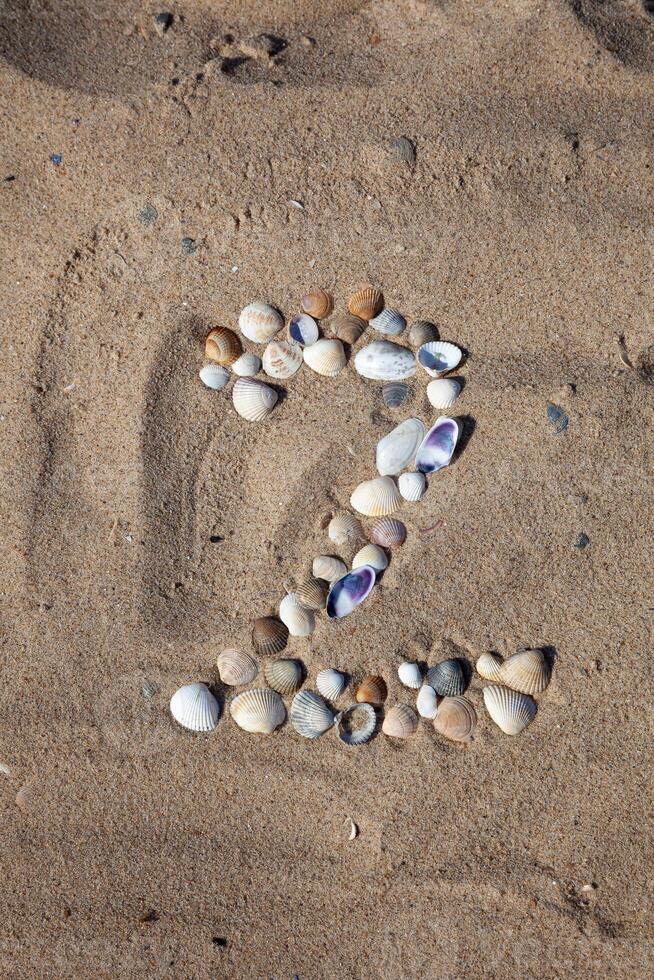 Number 2 laid out from seashells on the sand. Marine background. The symbol is two. Shells. photo