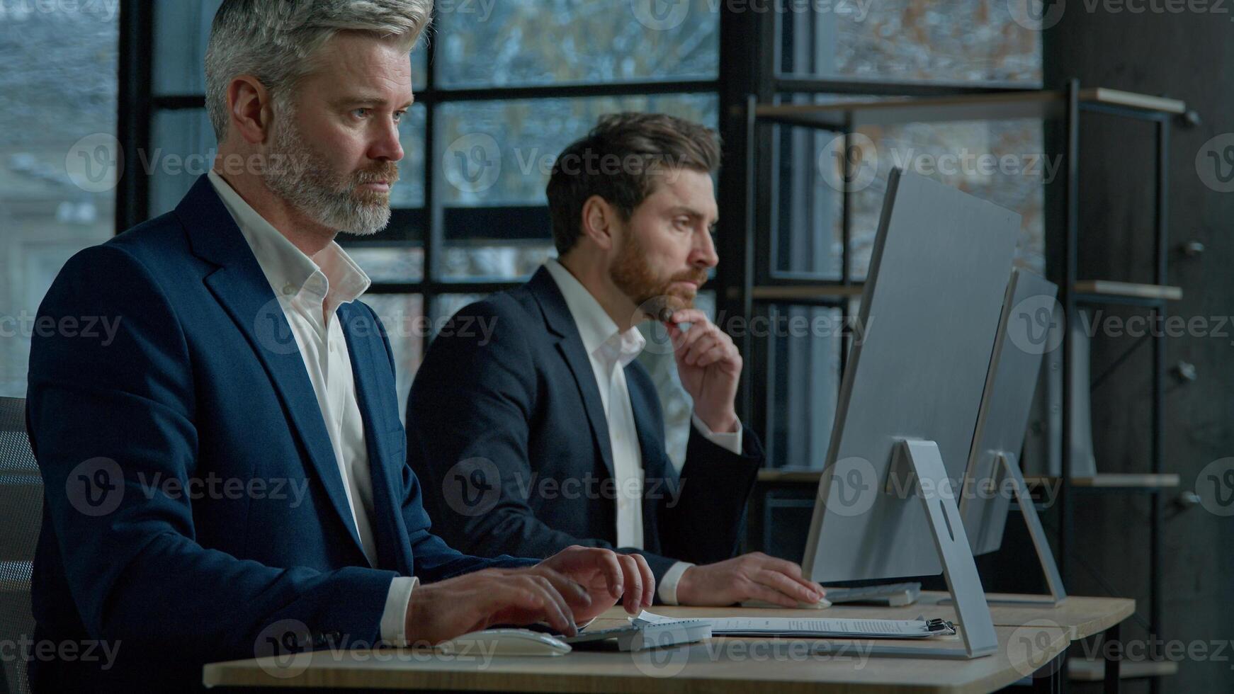 Focused professional managers working with computers on project sit in row at desk in office caucasian adult business men businessmen corporate employees colleagues work on Internet typing on computer photo