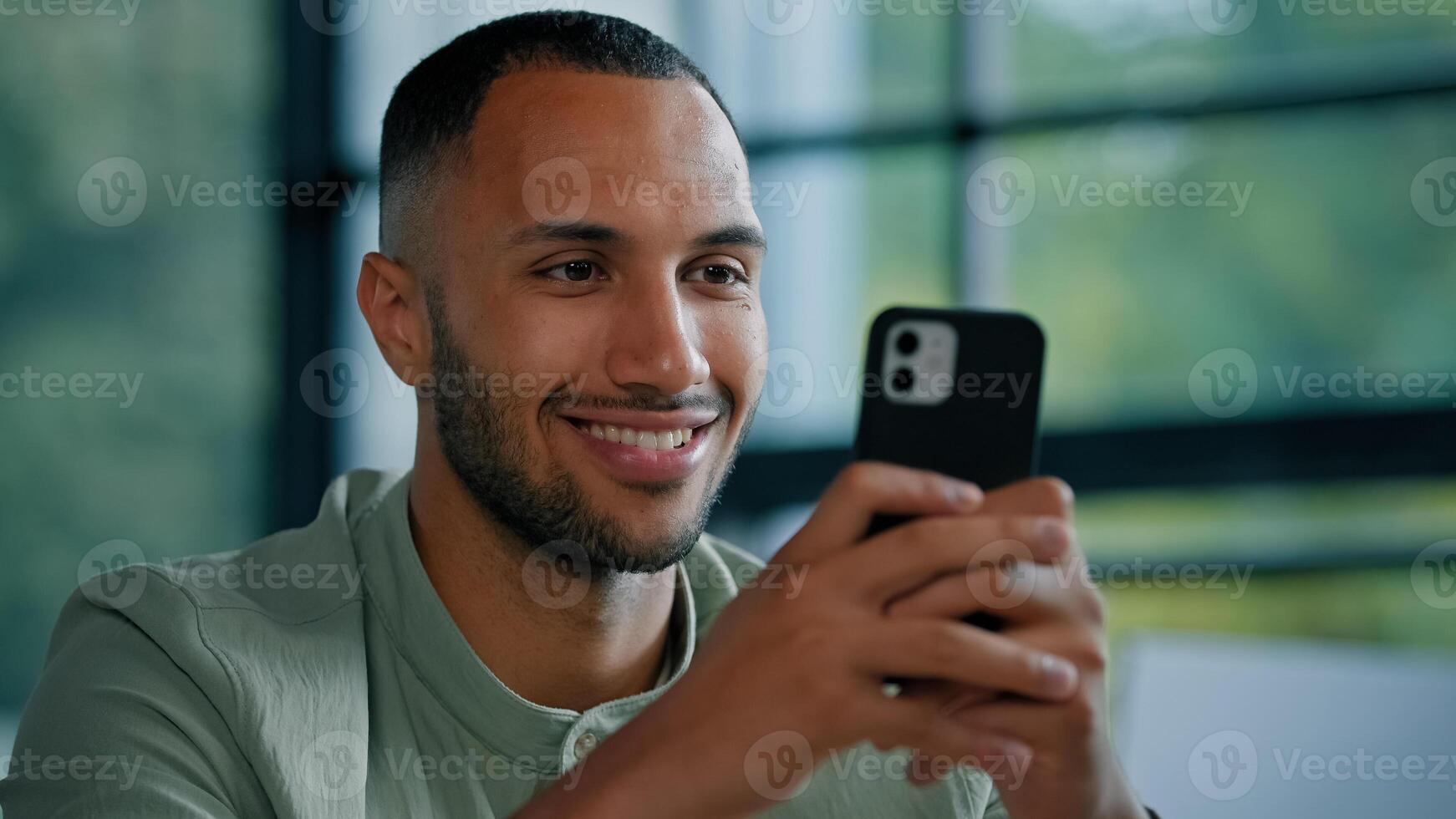 African American bearded man indoors using smartphone male employer entrepreneur businessman with phone sitting at office typing chatting with mobile app service browsing net online smile to camera photo