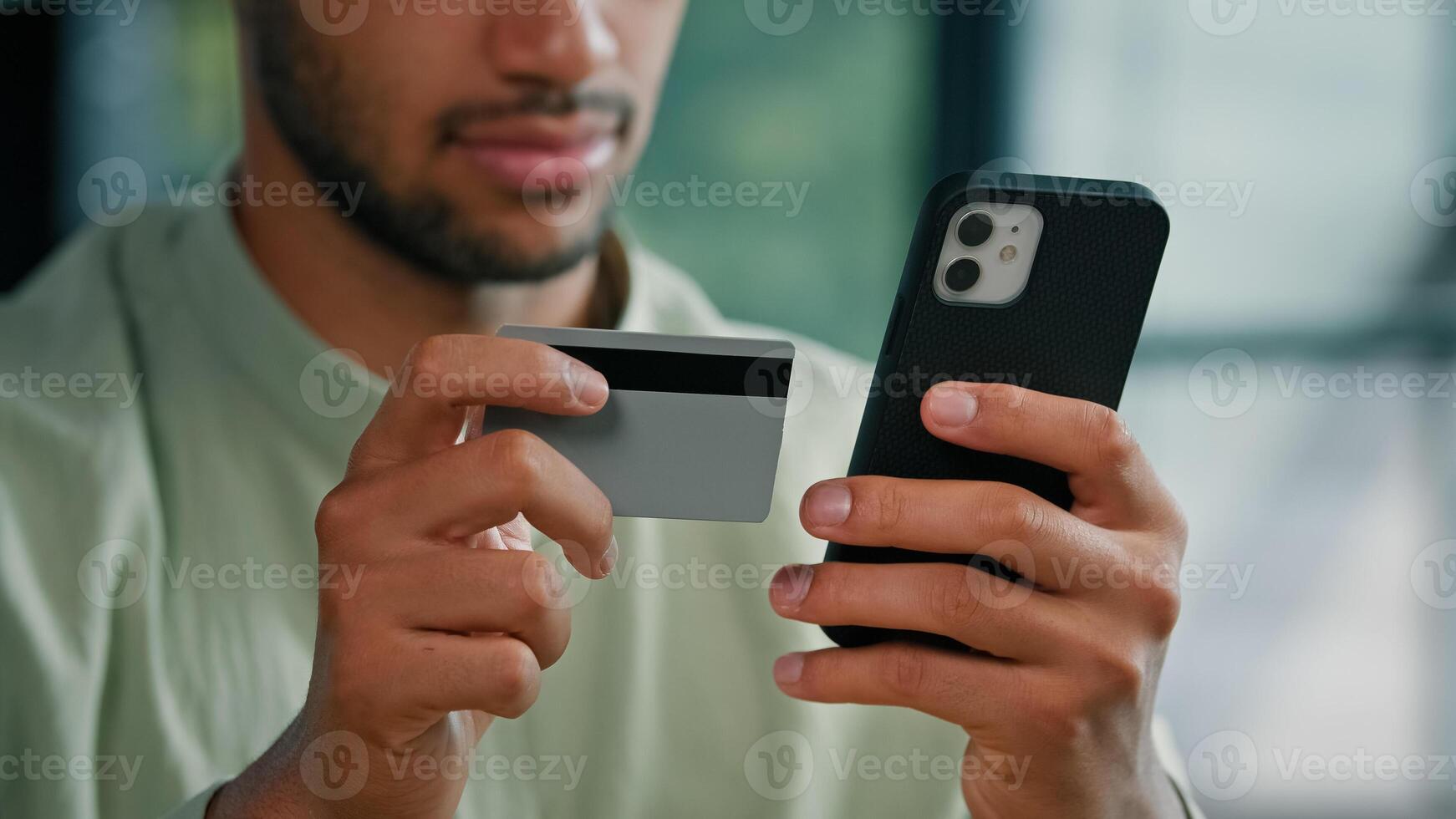 African American bearded man indoors unrecognizable male customer holding credit card and smartphone sitting at home office using easy mobile payment app service making purchase buying in online store photo