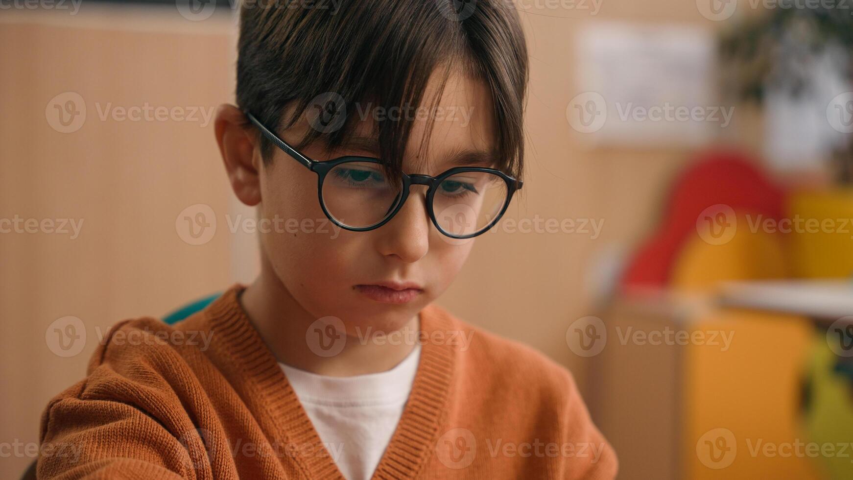 Close up portrait little sad upset frustrated son child kid pupil student boy in school class lesson elementary education writing test exam problem difficulties lonely studying learning study learn photo
