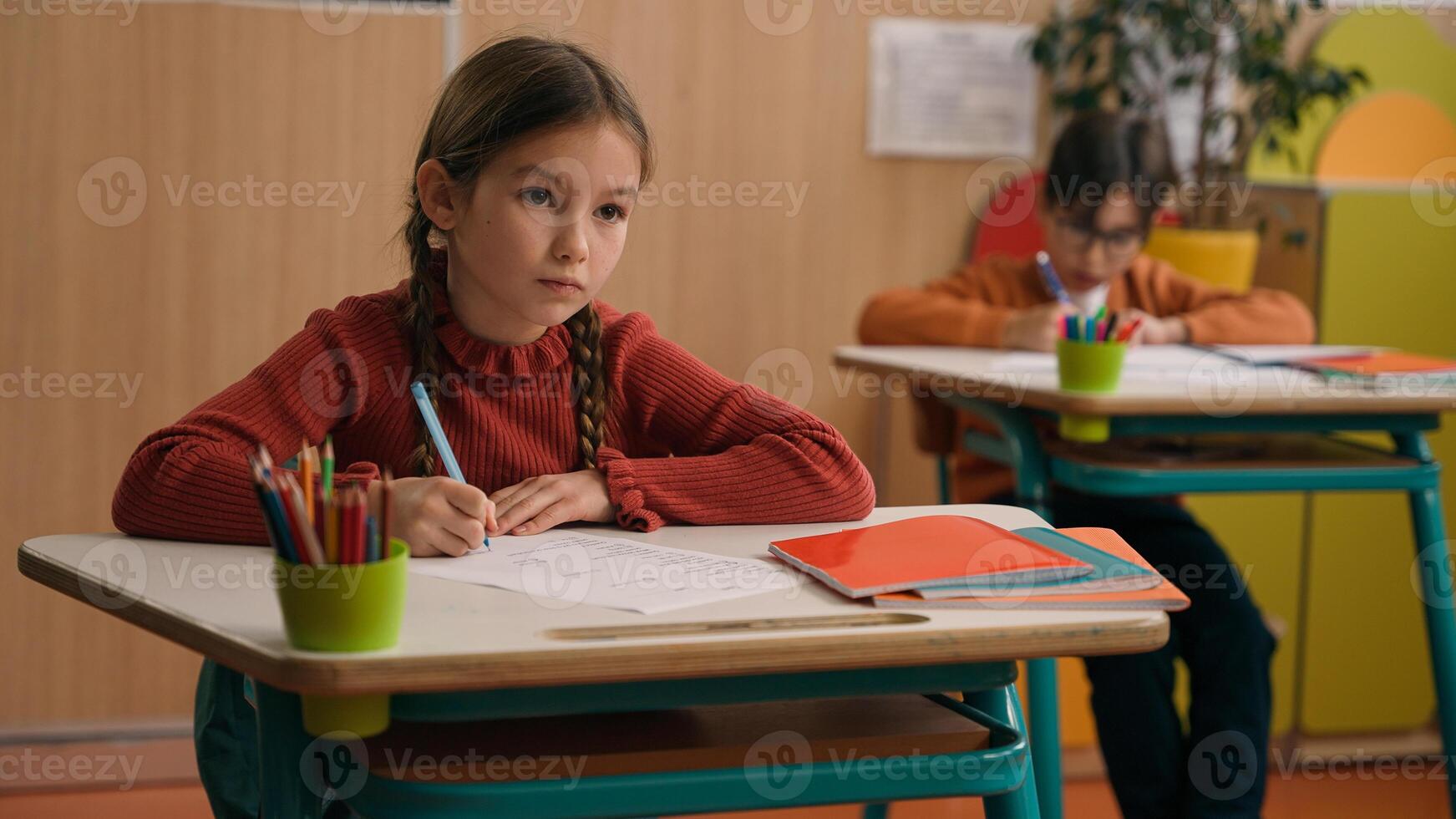 Concentrated Caucasian kid child schoolgirl primary school girl daughter pupil learn at classroom with classmates writing task write note class lesson study knowledge listen teacher studying education photo