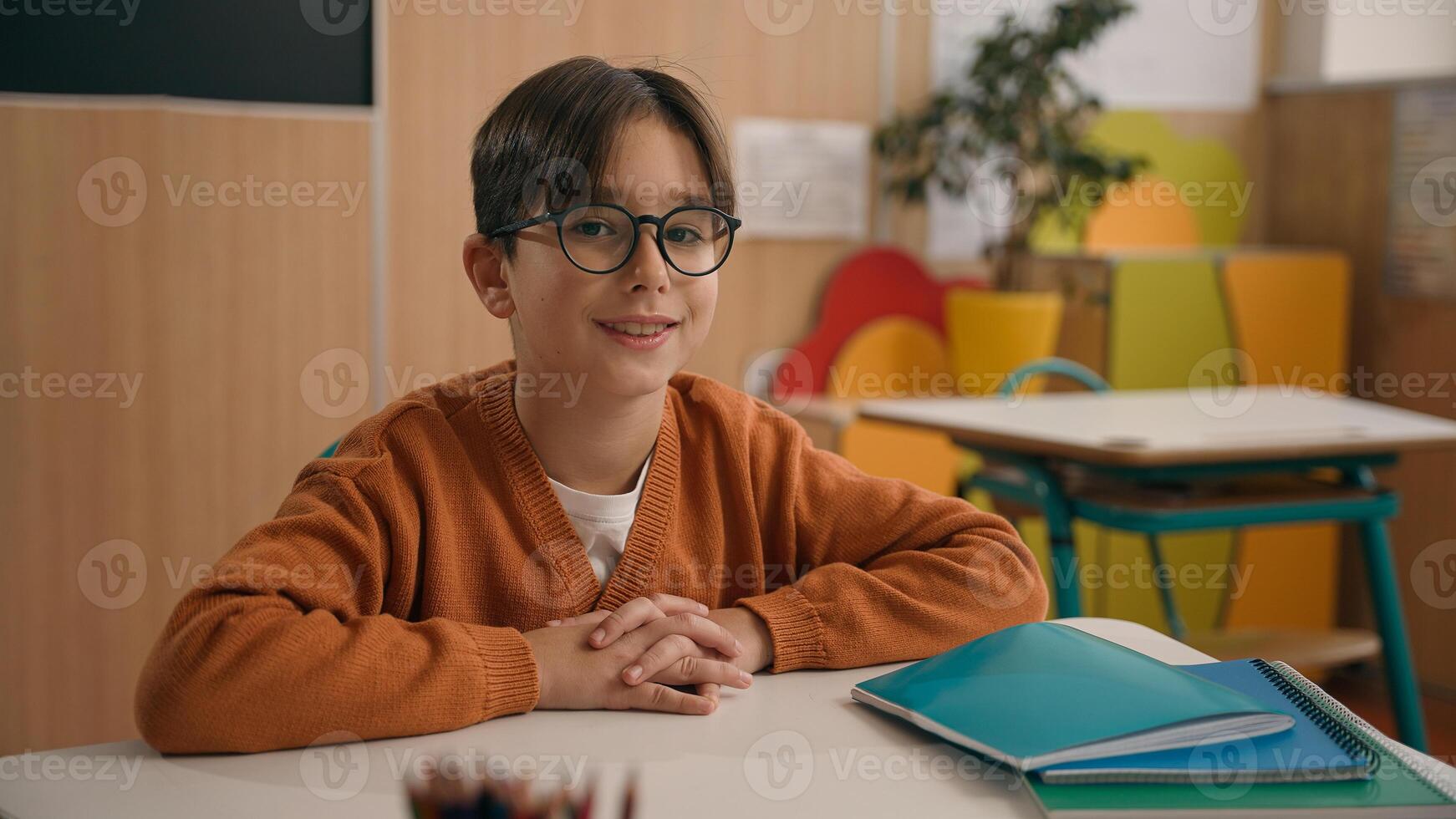 Portrait little smiling Caucasian boy in eyeglasses healthy son looking at camera sitting at table primary school classroom smile kid schoolboy child baby pupil student studying education at desk photo
