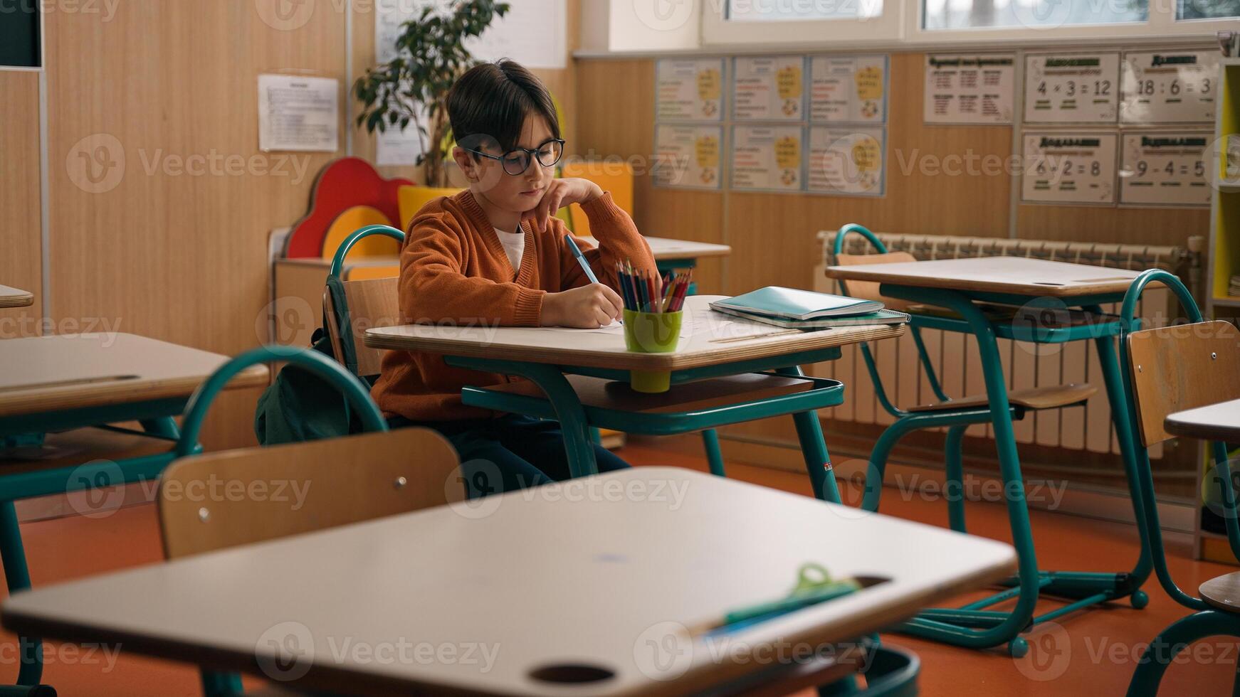 Alone little boy in empty school class room sitting at desk table writing homework clever Caucasian primary school child kid son pupil learning task write notes lesson studying elementary education photo