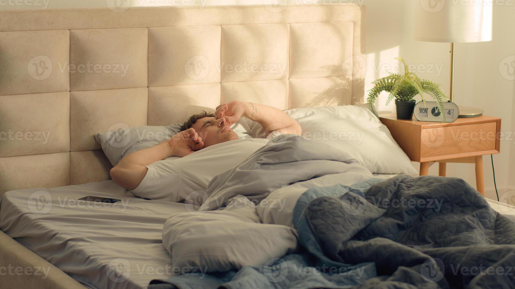 Caucasian man waking up stretching sleeping good morning bed bedroom home smiling satisfaction enjoy male weekend cozy daydream slumber napping tenant homeowner relaxed pulling pleasure apartment guy photo