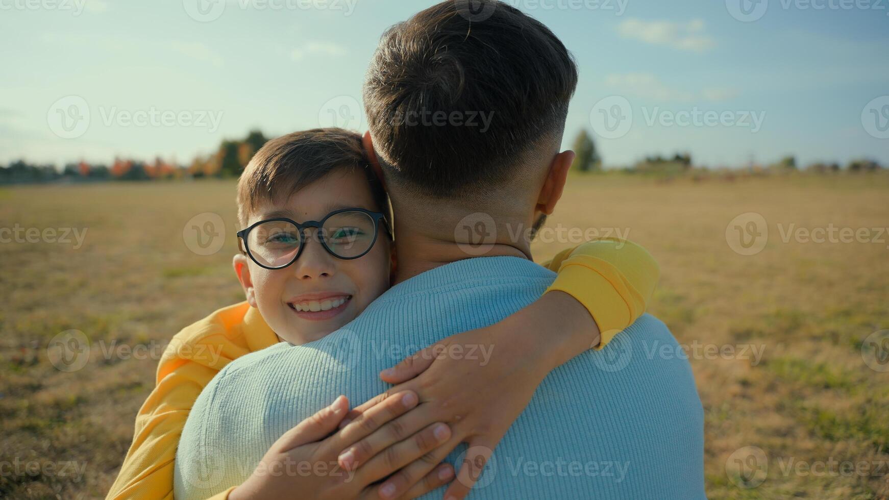 Happy Caucasian smiling little boy cute kid son hugging embracing cuddle foster parent man male dad father daddy hug adopted child loving family relationship adoption custody nature rural field meadow photo
