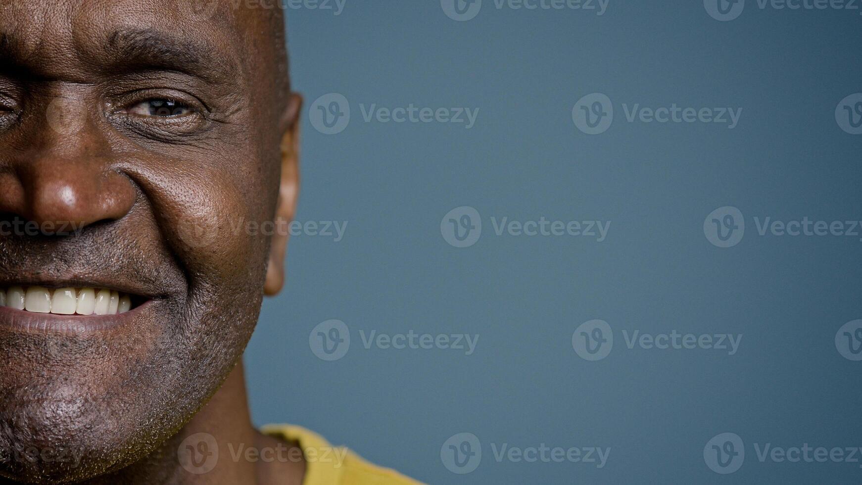 Close-up half male face with joyful expression mature african american man looking at camera smiling white healthy toothy smile happy customer satisfied with service posing in gray background studio photo
