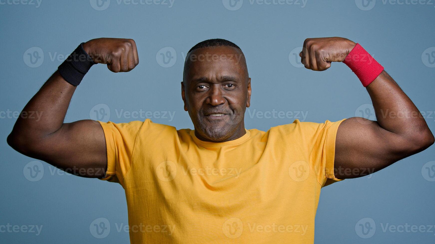 Portrait mature sports african man posing in studio gray background strong muscular athletic male athlete sportsman demonstrates biceps inflated triceps middle aged bodybuilder showing strong muscles photo