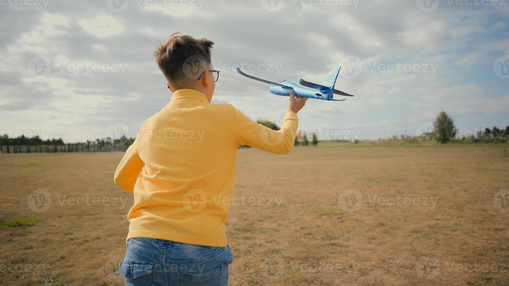 Back view happy Caucasian teen little boy child kid adopted son schoolboy enjoying summer holidays playing launching plane toy airplane flight dreaming to become a pilot travelling nature field meadow photo